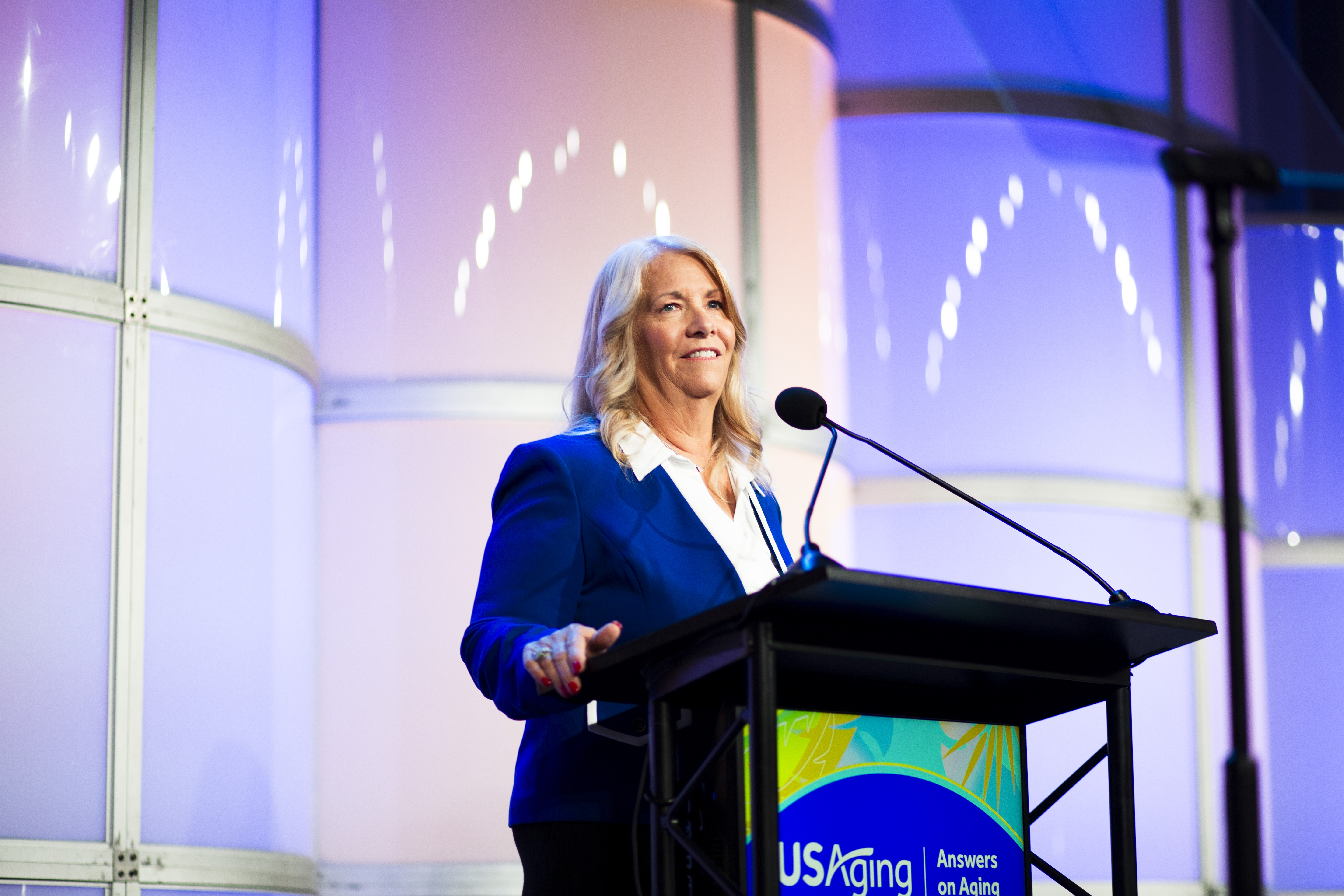 USAging President Duanna Patton stands at a podium on the stage of the General Session. Behind her are white cylindrical structures that serve as the stage backdrop.