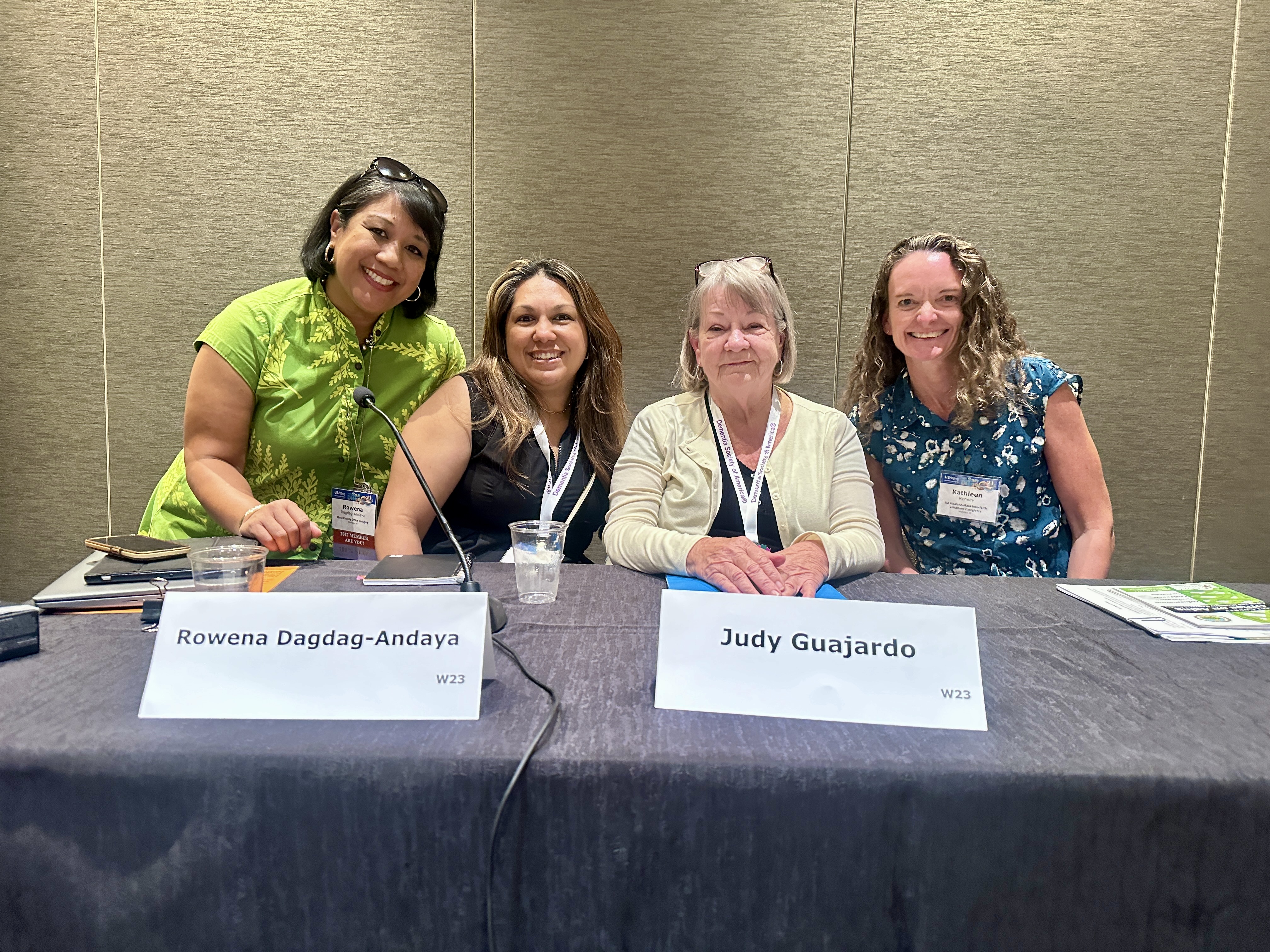 Four female session presenters smile while sitting behind their panelist table on stage. 